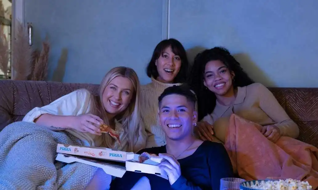 Amigos reunidos no sofá com pizza e pipoca para assistir à televisão